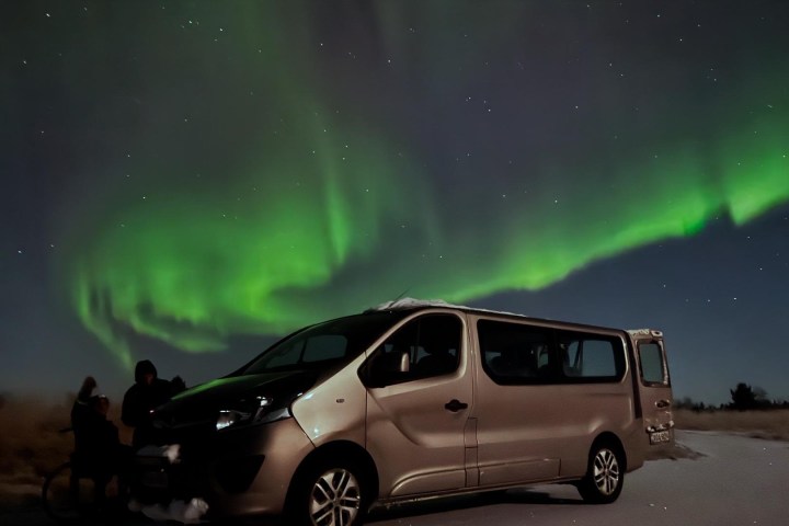 Van parked under green aurora lights in a starry night sky.