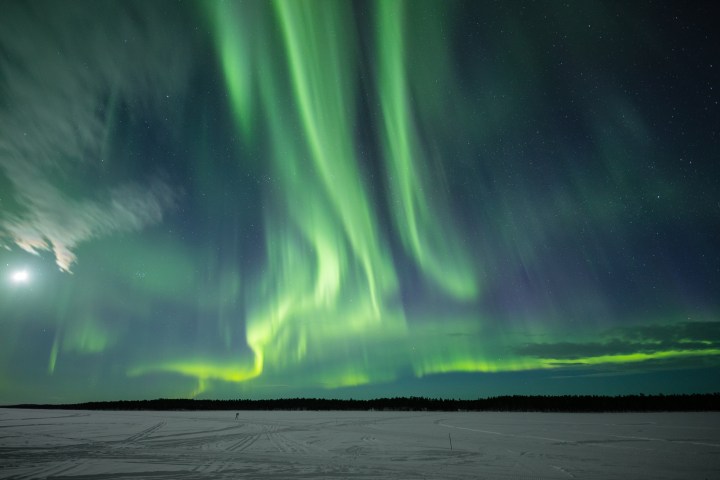 Vibrant green aurora lights dancing over a snowy landscape with a moon in the sky.
