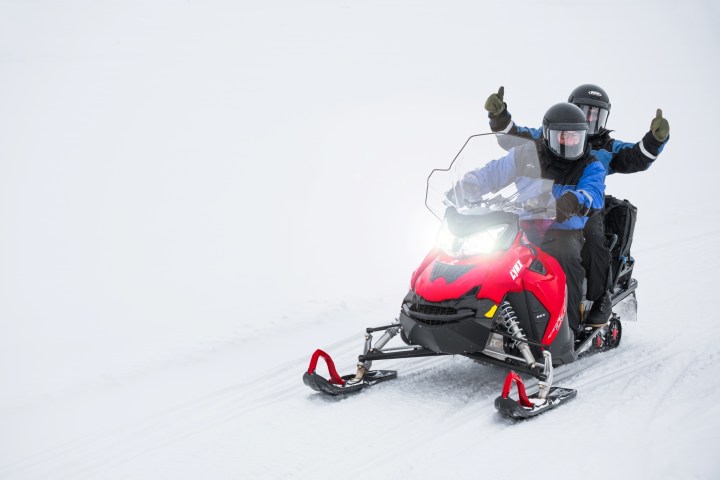 Two people riding a red snowmobile on a snowy landscape with thumbs up.