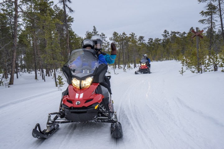 Two people riding a red snowmobile on a snowy forest trail.
