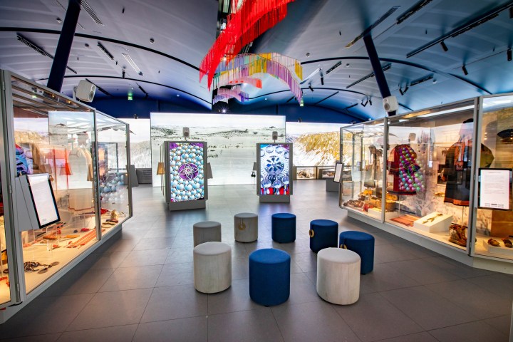 Modern museum exhibit with colorful displays, artifacts, and seating under a ceiling with hanging decorations.