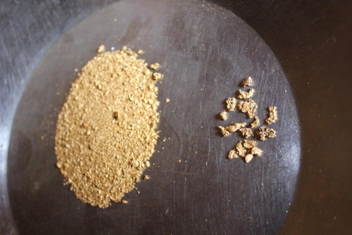 Gold dust and nuggets on a metallic pan surface.