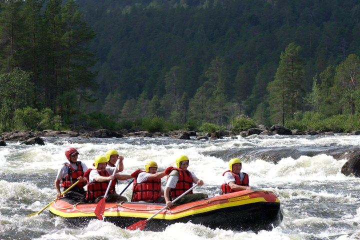 Group rafting on a river with rocky rapids and forested hills in background.