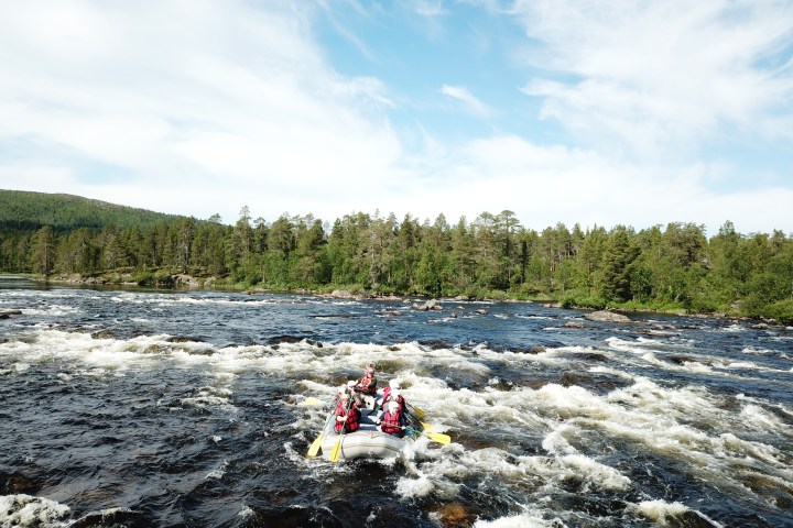 People rafting on a river with rapids and forested banks under a cloudy sky.
