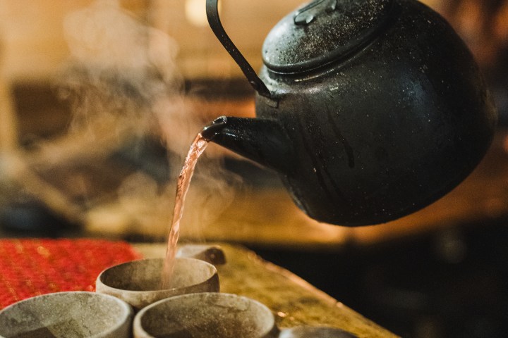 Person pouring hot beverage into cups from black kettle on a table.