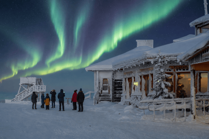People watch the Northern Lights near a snow-covered building.